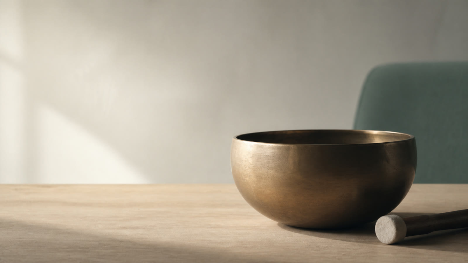 A brass singing bowl resting beside its mallet